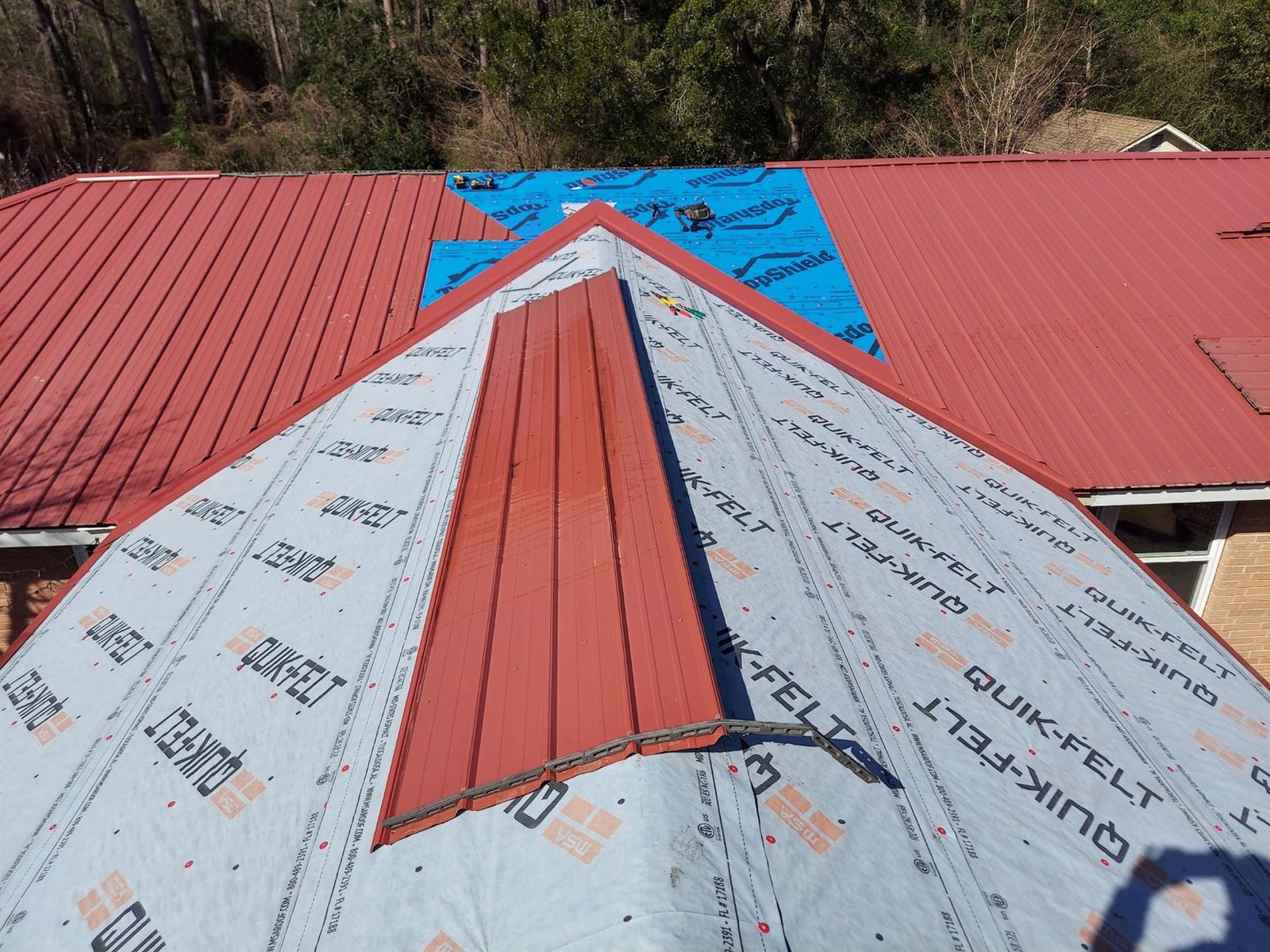 Red metal roof panels with underlayment visible during preparation